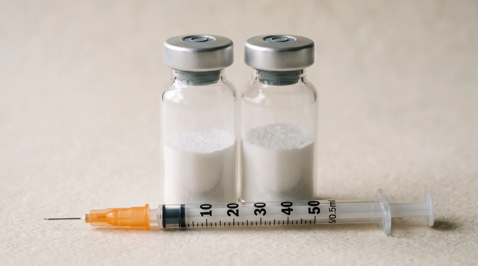 Illustration: two unlabelled glass vials of powder side by side with one insulin syringe lying in front of them.